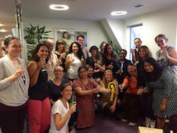 A group of people, mainly women, holding glasses of what looks like champaigne. One of them is holding a yellow rosette.