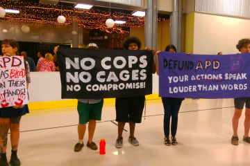 Activists from Underground Sketchbook hold banners and signs demanding funding cuts for the Austin Police Department at a community forum on race and policing on August 24, 2015. (MintPress News / Kit O’Connell)