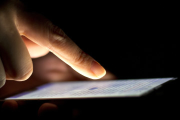 File: Close-up of a hand hovering above a smartphone in a dark room. (Flickr / Japanexperterna.se)