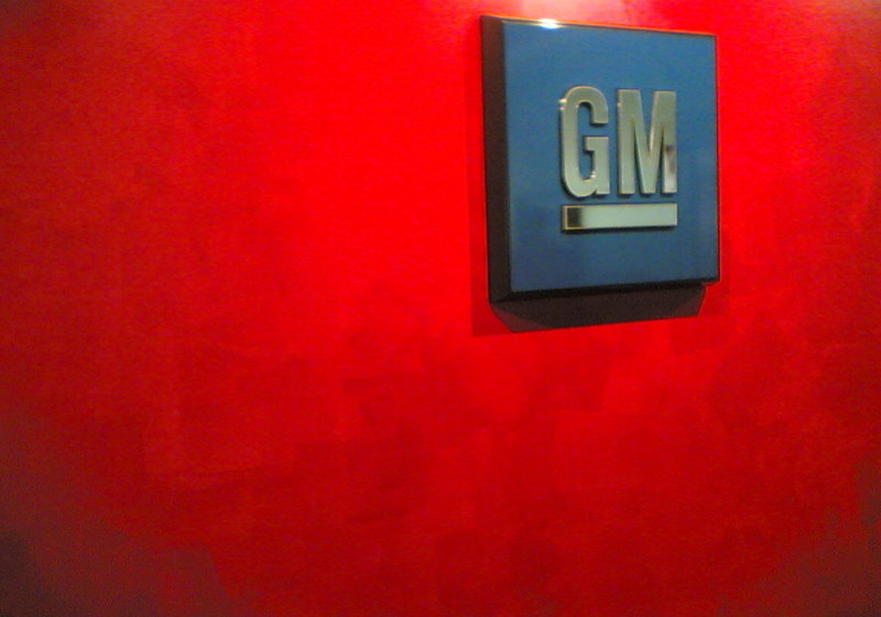 File: The GM logo badge from a vehicle against a red background. (Flickr / jm3 on Flickr)