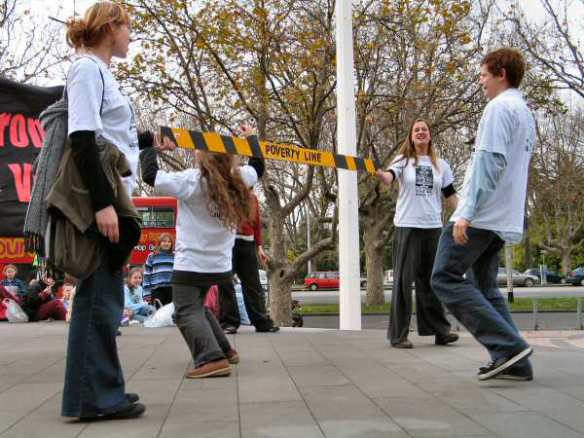 Students performing 'poverty line limbo' -under the yellow tape