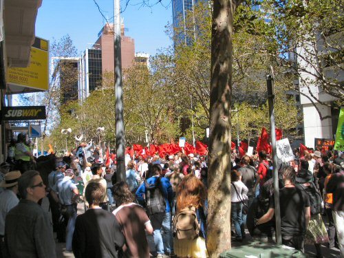 Red flags prominent in crowd filling street. 