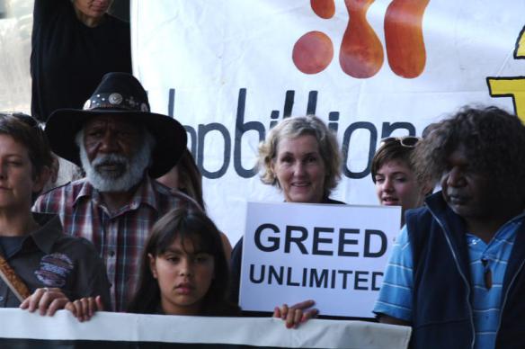 Elders and protesters with placard - Greed unlimited