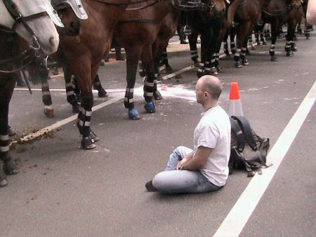 Man in lotus position facing line of mounted police