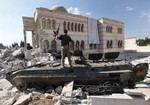 In this Sept. 23, 2012, file photo, a Free Syrian Army soldier stands on a damaged Syrian military tank in front of a damaged mosque, which were destroyed during fighting with government forces, in the Syrian town of Azaz, on the outskirts of Aleppo.