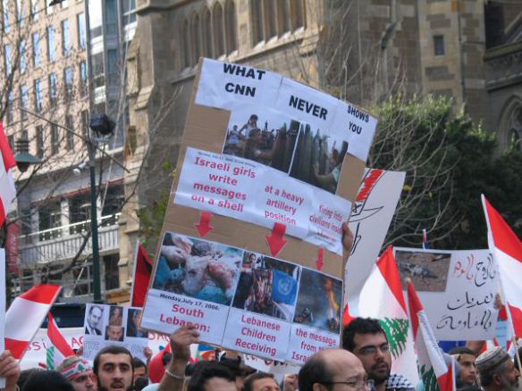 The upper part of the placard has photos of Israeli children chalking mesages on shells about to be fired into Lebanon