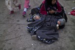 An Afghan refugee woman sits on the ground with her twin sons, Othman Abdulghafar, 2, right, and Irafan, sleeping by wrapped with a blanket to shelter from the morning cold after spending the night at a collection point in the truck parking lot of the former border station on the Austrian side of the Hungarian-Austrian border near Nickelsdorf, Austria, Friday, Sept. 25, 2015. Deeply divided European Union leaders held an emergency summit to seek long-term responses to the continent's ballooning crisis of refugees and migrants, a historic challenge EU President Donald Tusk said the bloc has failed dismally to meet.