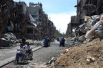 File - In this picture provided by the United Nations Relief and Works Agency for Palestine Refugees in the Near East (Unrwa.org), two men on their wheelchairs, wait to receive food supplies at a damaged street in the besieged Yarmouk refugee camp, on the southern edge of the Syrian capital Damascus, Syria, Thursday April 24, 2014.