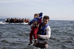 A Syrian refugee carries his child after they arrived from Turkey to the shores of the Greek island of Lesbos, on an inflatable dinghy, with another boat in the background, Saturday Sept. 26, 2015.