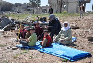 In this picture taken on Saturday April 18, 2015, a displaced Kurdish family sit in the open air field near their house which was destroyed during the battle between the U.S. backed Kurdish forces and the Islamic State fighters, in Kobani, north Syria.