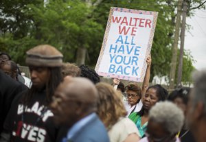 File - Lisa Eberle, of Charleston, S.C., holds a sign while observing a moment of prayer during a vigil at the scene where Walter Scott was fatally shot by a white police officer after he fled a traffic stop, Sunday, April 12, 2015, in North Charleston, S.C.