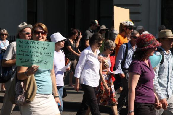 Woman in crowd arriving - placard reads 'I'm supporting the carbon tax because I actually care about out planet and our kids' future'