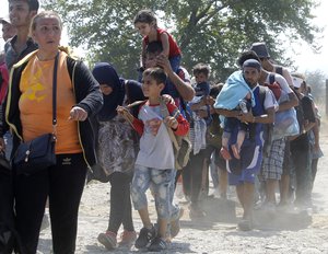 A group of migrants walk along a dusty road towards the transit center for migrants, after crossing the border from Greece to Macedonia, near southern Macedonian town of Gevgelija, on Monday, Aug. 31, 2015.