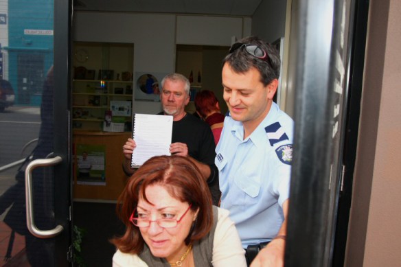 Staffer reaches across to close door. Dave Sweeney holds up petition inside office.