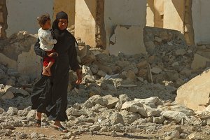 File - An Iraqi woman holds her child as she walks through the rubble in a displaced citizen’s camp in Mosul, Iraq, April, 17, 2008.