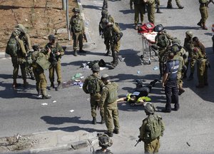 File - Israeli soldiers stand around the body of a Palestinian, seen on the ground, who was shot and killed after stabbing an Israeli soldier during clashes in Hebron, West Bank Friday, Oct. 16, 2015.