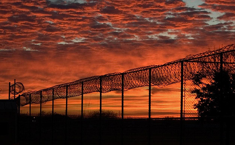 A sunset seen through a prison fence topped with barbed wire. (Bureau of Prisons)