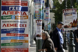 An elderly woman begs next to banners announcing tomorrow's general strike in Athens, Greece, Wednesday, Nov. 11, 2015.