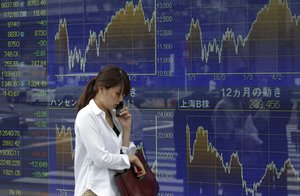 A woman speaks on a mobile phone in front of a securities firm's electronic stock board in Tokyo Monday, June 25, 2012.