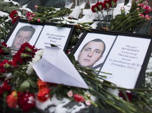 Photos of Lt.Col. Oleg Peshkov, left, and sailor Alexander Pozynich are placed at a monument to Soviet Officers with flowers and a toy jet made of paper outside Russian Army General Staff headquarters in Moscow, Russia, Thursday, Nov. 26, 2015.