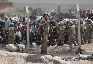 Turkish soldiers guard the damaged border fence while Syrian refugees mass at the Turkish border as they flee intense fighting in northern Syria between Kurdish fighters and Islamic State militants in Akcakale, southeastern Turkey, Monday, June 15, 2015.