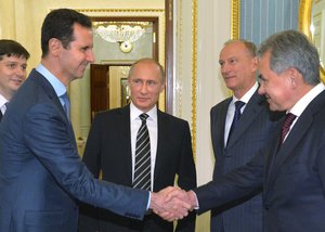 In this photo taken on Tuesday, Oct. 20, 2015, Syrian President Bashar Assad, second left, shakes hand with Russian Defense Minister Sergei Shoigu, as Russian President Vladimir Putin, center, looks on in the Kremlin in Moscow, Russia.