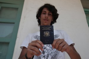 Syrian refugee Mouradin, 16, last name not given, holds his Syrian passport, as he waits to be registered outside the local coast guard building in the Greek island of Leros, Monday, Aug. 17, 2015.