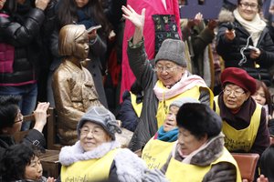 A former South Korean comfort woman Kil Un-ock, right, who was forced to serve for the Japanese Army as a sex slave during World War II, reacts with other comfort women near the statue symbolizing a wartime sex slave during their 1,000th weekly rally to demand an official apology and compensation from the Japanese government in front of the Japanese Embassy in Seoul, South Korea, Wednesday, Dec. 14, 2011.