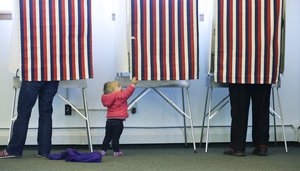 Zoe Buck, a 14-month-old child, checks out an empty voting booth as at her mother, Julie Buck, votes at left, Tuesday Nov. 4, 2014, at the Alaska Zoo polling place in Anchorage, Alaska.