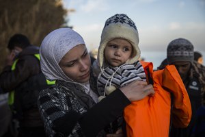 A woman takes off a life vest from a baby, shortly after crossing the Aegean sea on a dinghy, with other refugees and migrants, from Turkey to the Greek island of Lesbos, on Friday, Dec. 25, 2015.