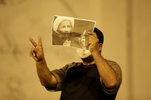 File - A Bahraini anti-government protester, masked against tear gas, gestures as he holds up a picture of jailed Saudi Sheik Nimr al-Nimr during clashes with riot police in Sanabis, Bahrain, a suburb of the capital Manama, Wednesday night, Oct. 15, 2014.