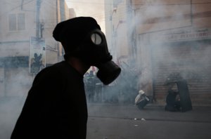 A Bahraini anti-government protester, masked against tear gas, watches riot police during clashes demanding freedom for jailed activists in Bilad Al Qadeem, Bahrain, Friday, Jan. 30, 2015.