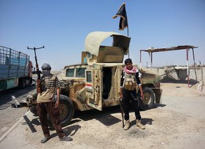 In this file photo taken Thursday, June 19, 2014, Islamic State group militants stand by a captured Iraqi army Humvee at a checkpoint outside Beiji refinery, some 250 kilometers (155 miles) north of Baghdad, Iraq.