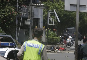 Bodies are seen as a police officer walks near the site where an explosion went off in Jakarta, Indonesia, Thursday, Jan. 14, 2016.