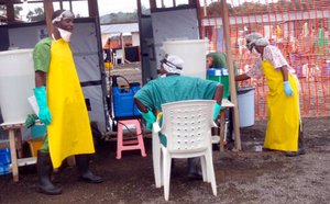 File - Surrounded by Ebola patients, a health worker, center, gives thumb-ups to visitors near the hot zone in West Africa, Sept. 26, 2014. The hot zone is defined by the double barrier orange fence in the event a sick person falls, they cannot contaminate the clean zone.