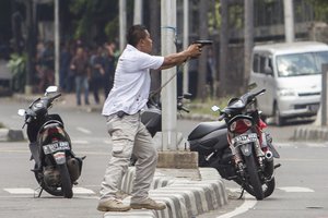 A plainclothes police officer aims his gun at attackers during a gun battle following explosions in Jakarta, Indonesia Thursday, Jan. 14, 2016.