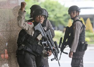 In this Thursday, Jan. 14, 2016, file photo, a police officer gives a hand signal to a squad mate as they search a building after an explosion in Jakarta, Indonesia.