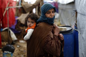 In this Monday, Jan. 4, 2016, file photo, a Syrian refugee carries a baby on her back at a refugee camp in the town of Hosh Hareem, in the Bekaa valley, east Lebanon.