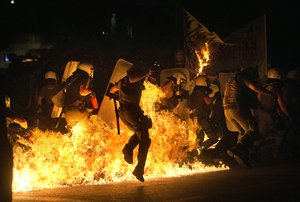 Riot police officers run through fire as anti-austerity protesters throw petrol bombs, during clashes in Athens, Wednesday, July 15, 2015.