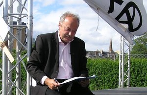 File - George Galloway signing an asylum seekers petition, sitting on the edge of the Stop The War Coalition stage at the 2005 Make Poverty History rally.