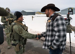 File - Ammon Bundy, right, shakes hand with a federal agent guarding the gate at the Burns Municipal Airport in Oregon on Friday, Jan. 22, 2016.