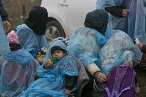 File - A migrant child and others covered with a plastic sheet to keep dry, rest during their walk from the Macedonian border into Serbia, near the village of Miratovac, Serbia, Wednesday, Jan. 6, 2016.