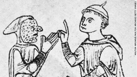 A leper, his face covered in sores, approaches a seated man with a gesture of supplication, circa 1200. From a manuscript by early medical writer Roger of Salerno. (Photo by Hulton Archive/Getty Images)