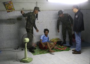 In this Monday, Nov. 9, 2015 photo, Thai soldiers and a member of the Department of Special Investigation wake up a worker during a raid on a shrimp shed in Samut Sakhon, Thailand. Thailand's government said on Monday, Dec. 21, 2015, that it is not ignoring the prevalence of slavery and forced labor in its lucrative shrimp industry.