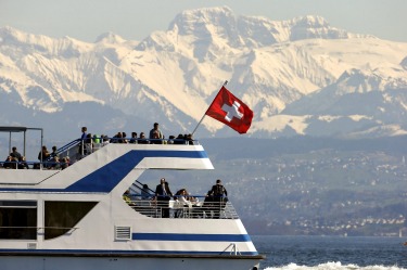 People enjoy the sunny spring weather aboard a tourist vessel sailing in front of the eastern Swiss Alps on Lake Zurich.