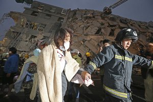 A woman is led by a rescue worker from the site of a toppled building after an earthquake in Tainan, Taiwan, Saturday, Feb. 6, 2016.