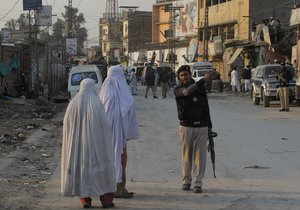 File: A Pakistani police officer directs women away from the site of a grenade attack ...