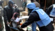 UN relief worker gives food supplies to Palestinian woman at the gate of the besieged Yarmouk refugee camp, Damascus, Feb. 4, 2014.