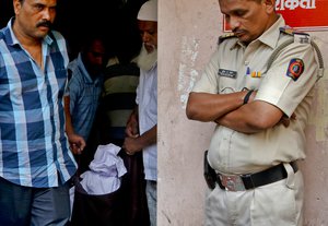 A police officer stands outside a morgue as relatives carry the body of one of the victims fatally stabbed by a man in Thane, outskirts of Mumbai, India, Sunday, Feb. 28, 2016.