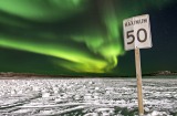 The northern lights illuminate the night sky above a road sign in Inuvik. 